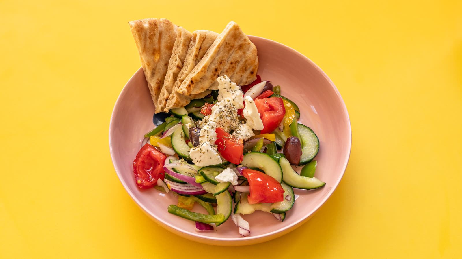 Salade grecque dans un bol rose, avec des triangles de pita