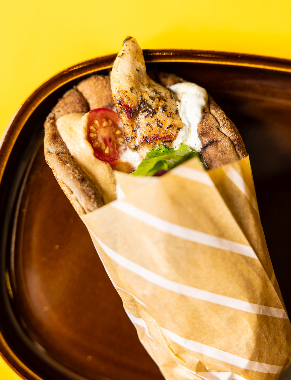 Wrap souvlaki au poulet dans une pita au blé complet, avec tzatziki, tomate et salade, dans son papier rayé